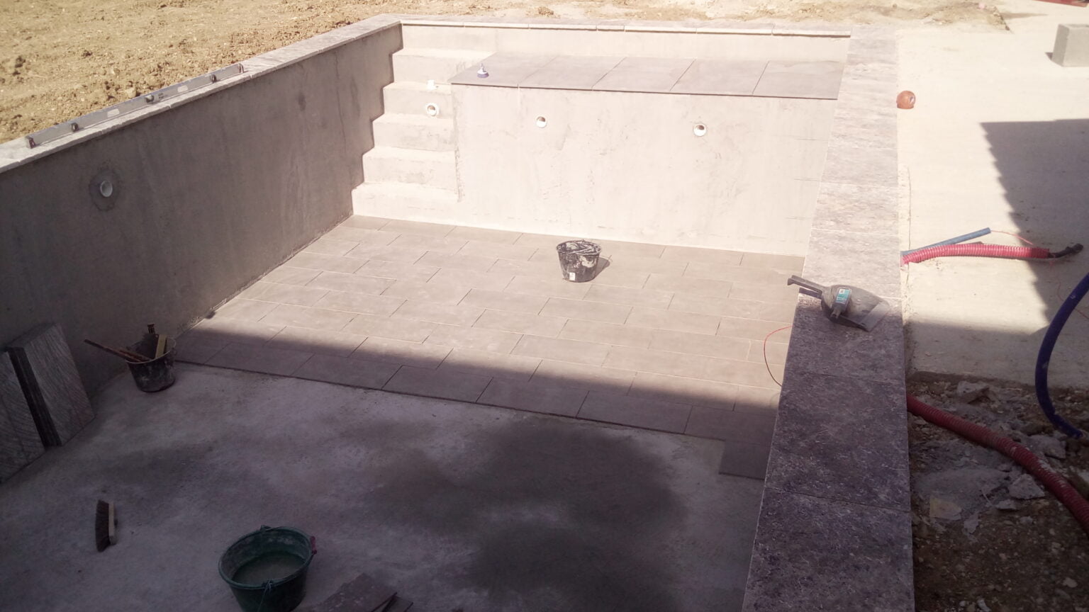 Piscine béton terminée : carrelage de fond, escalier maçonné et margelles en pierre posées