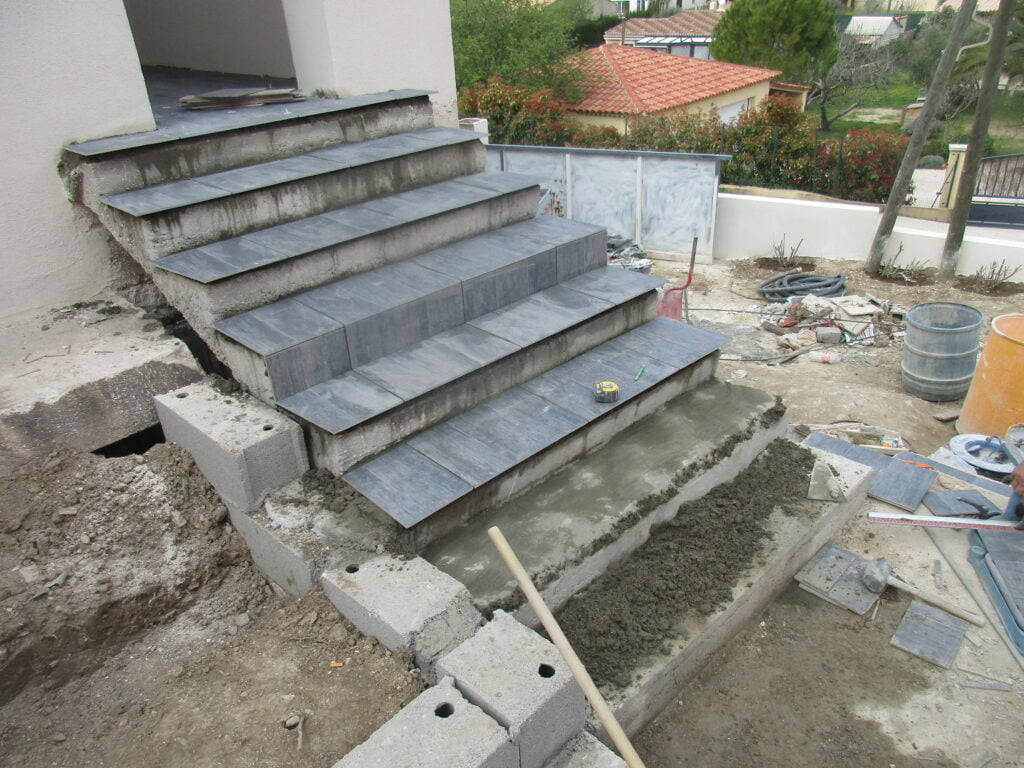 Escalier extérieur en béton en cours d'habillage avec des marches en pierre bleue