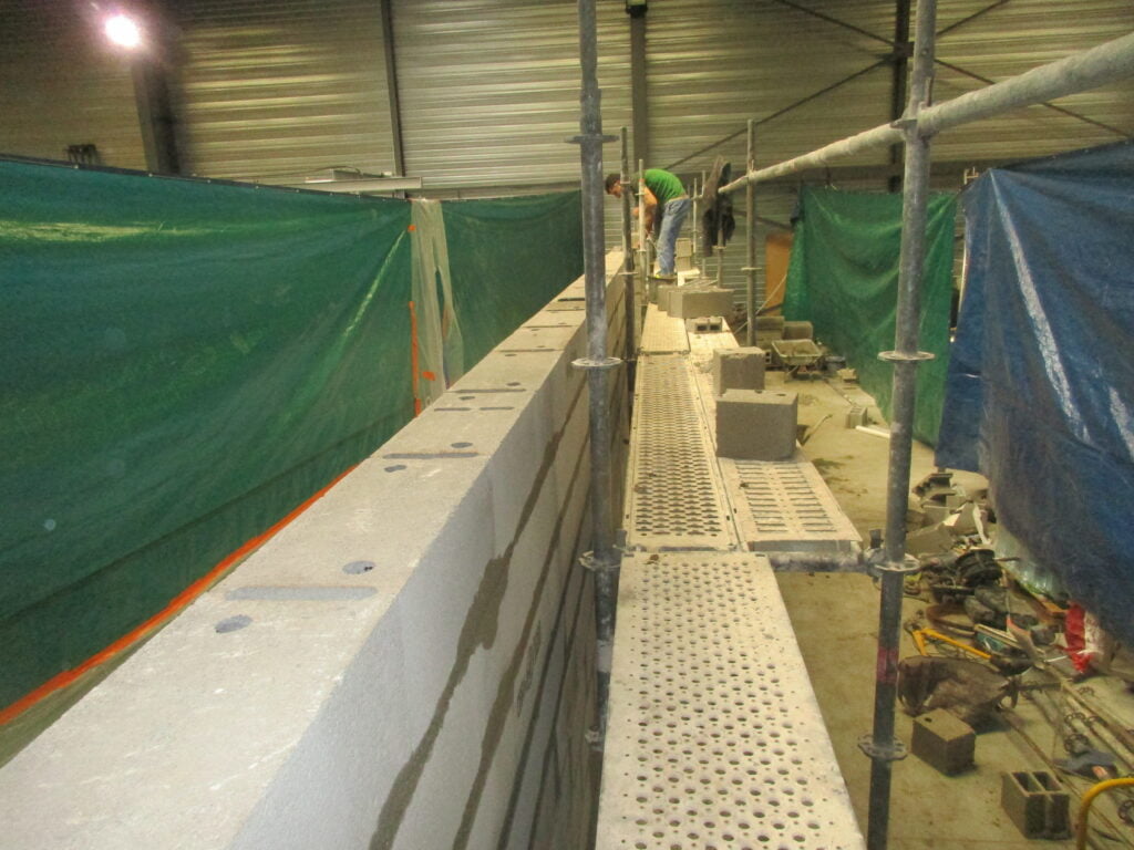Mur en blocs béton monté sur échafaudage à l'abri d'un hangar, arase soignée