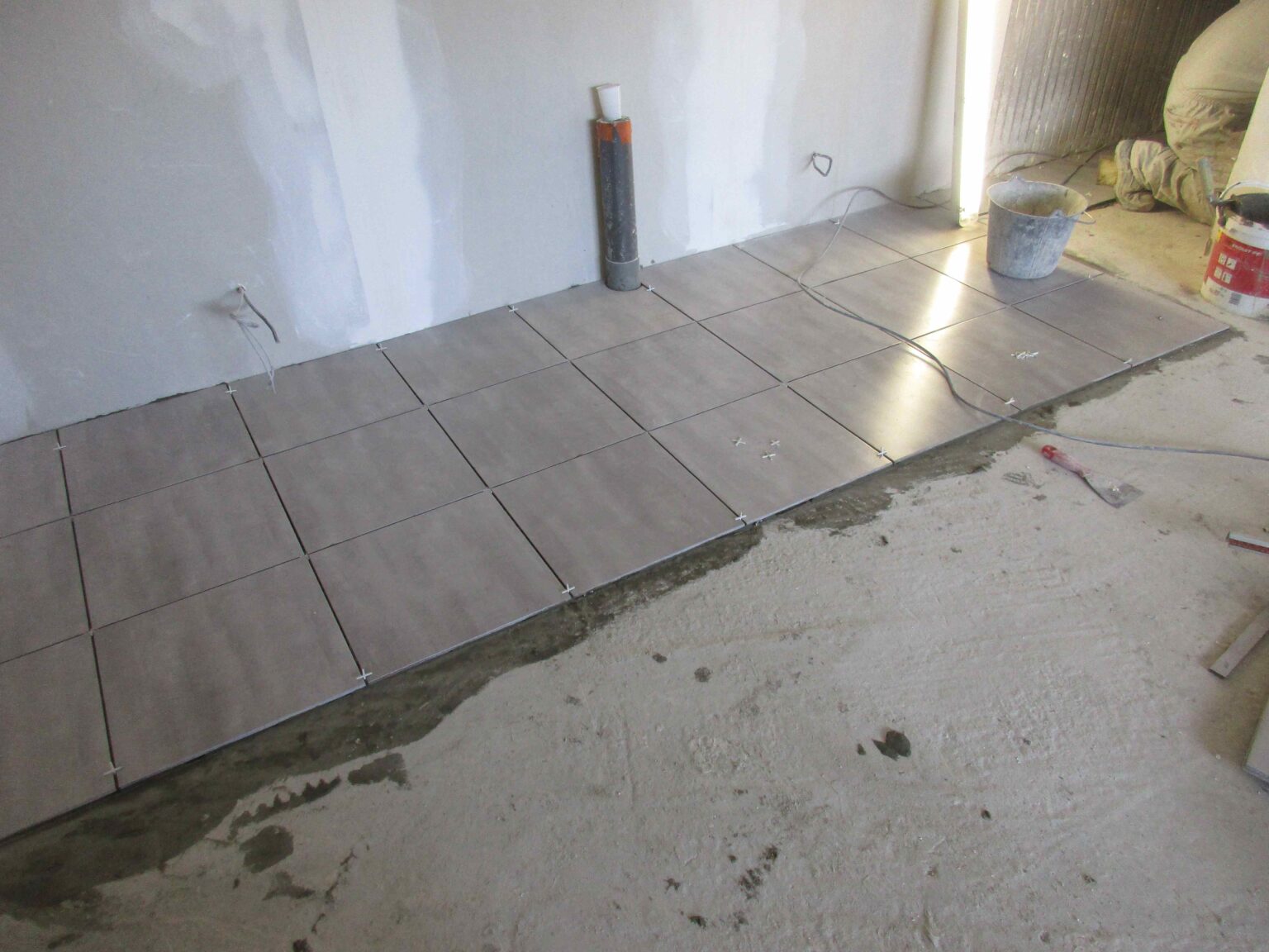 Carrelage de sol en cours de pose, attente d'évacuation en PVC contre le mur