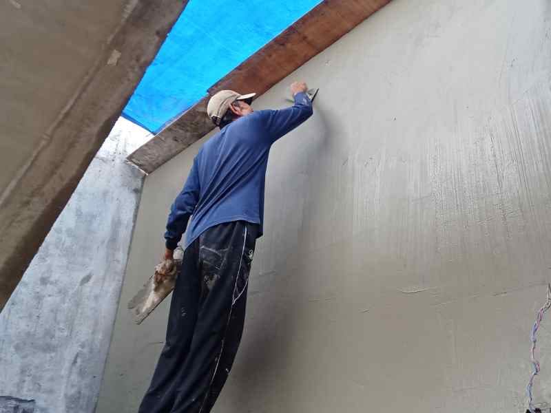 Ouvrier sur un échafaudage en train de reprendre une fissure en façade et appliquer le marouflage