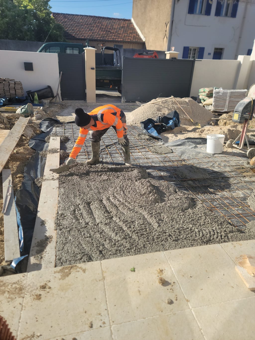 Maçon tirant le béton à la règle alu — coulage dalle Saint-Barnabé
