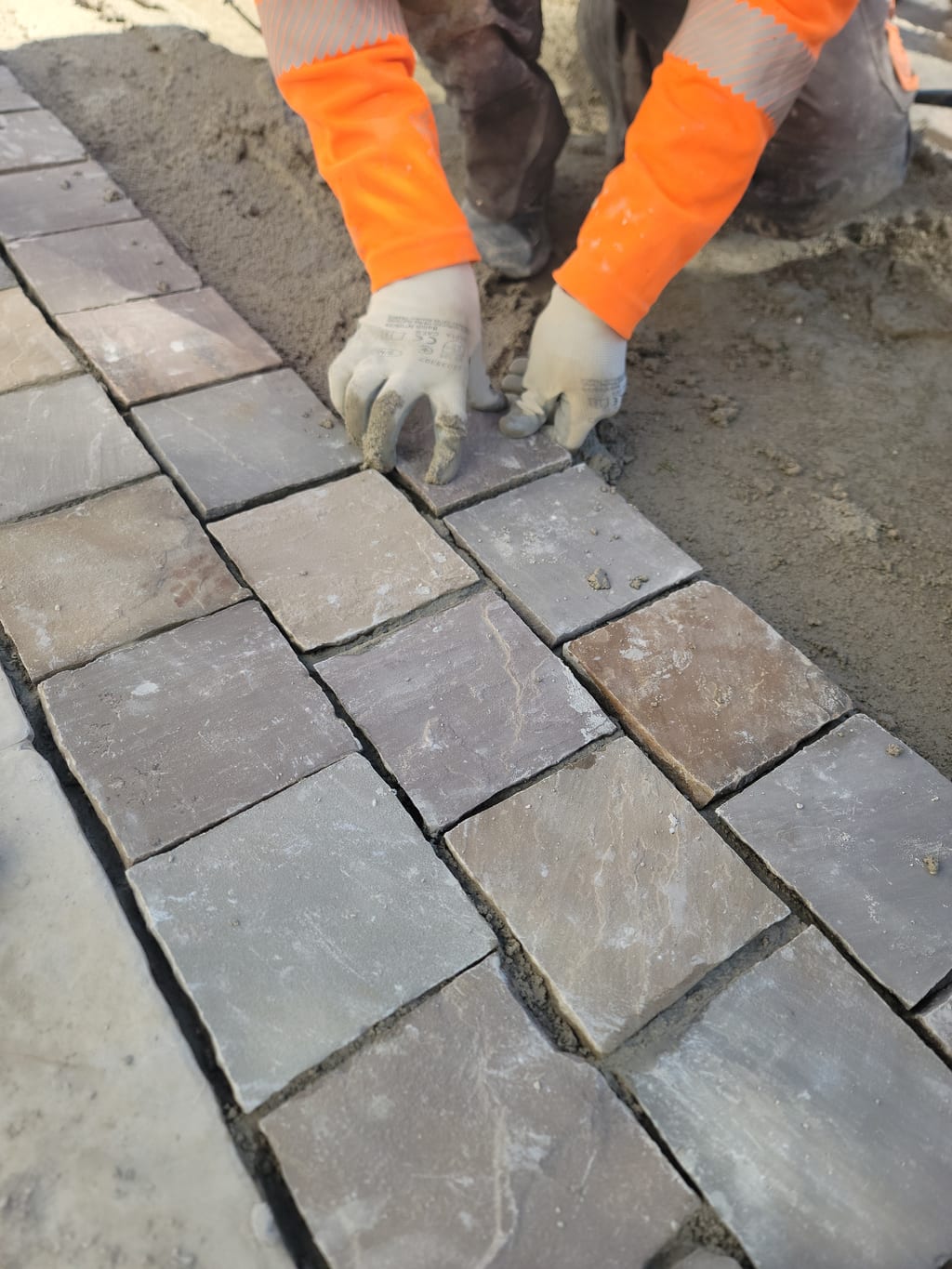 Mains gantées posant un pavé multicolore — détail pose