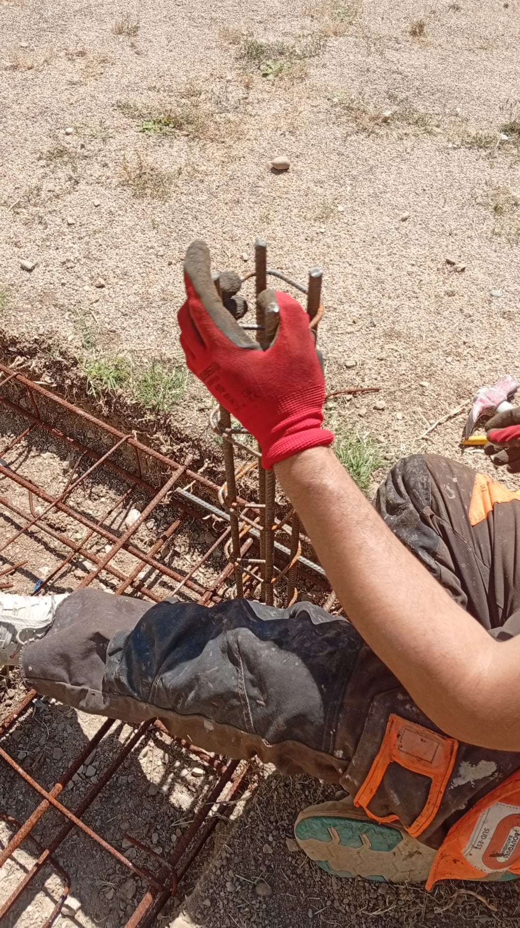 Façonnage de l'armature acier de la fondation d'une clôture avant coulage du béton, chantier de maçonnerie