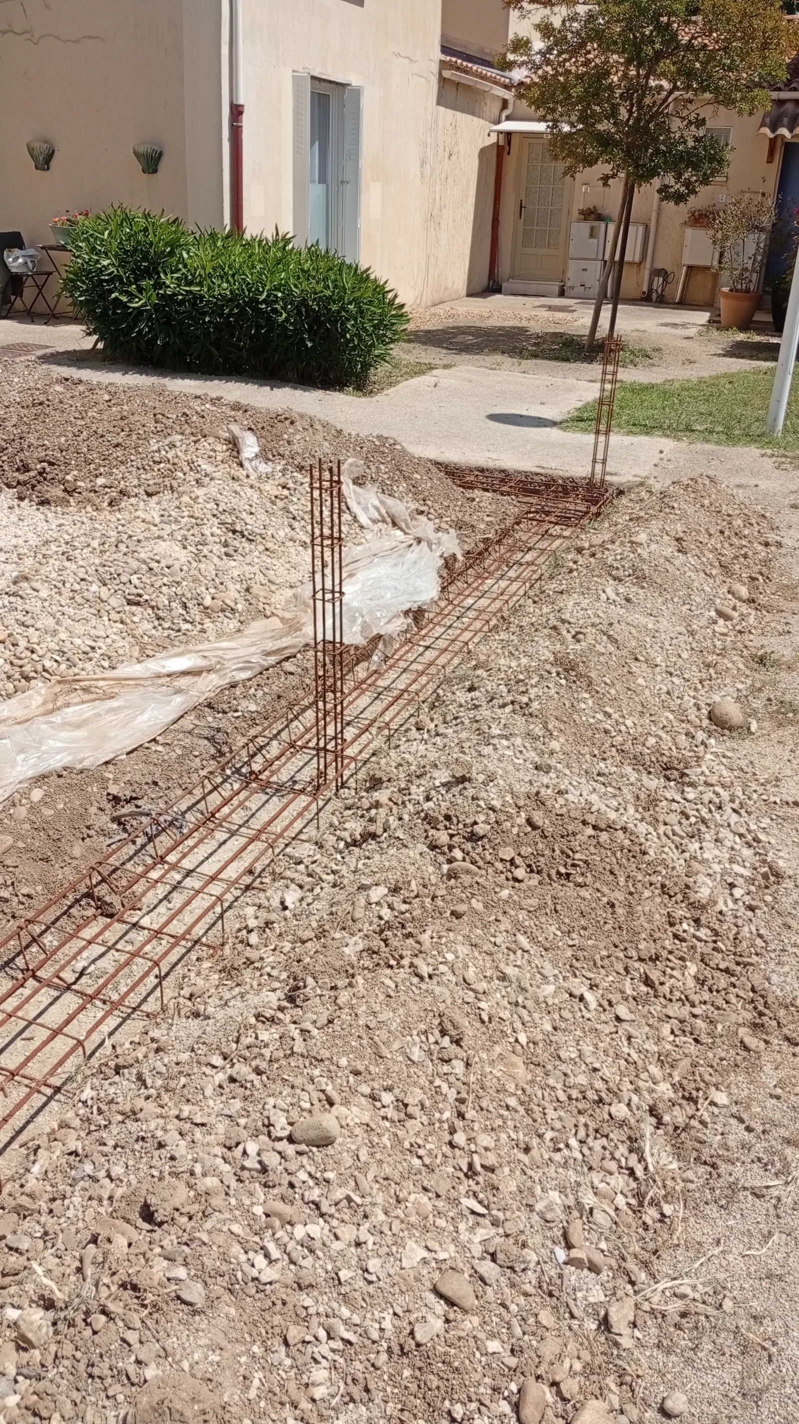 Fondation ferraillée avec poteau raidisseur en attente, première étape de pose d'un grillage sur soubassement
