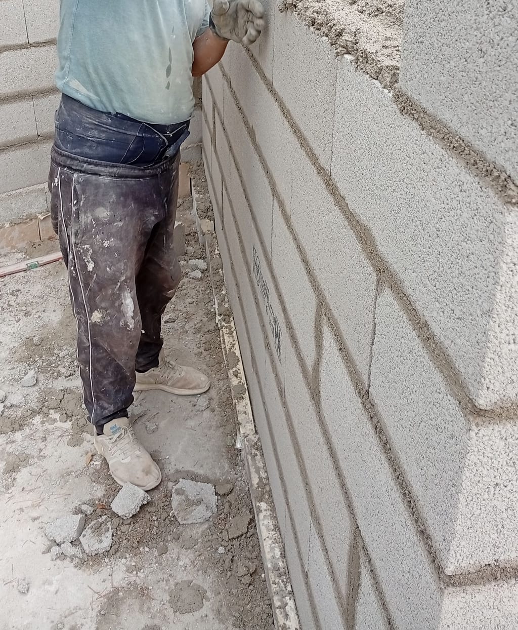 Maçon posant un bloc d'agglo à la truelle sur le mur d'une extension à toit plat — chantier Marseille 13008