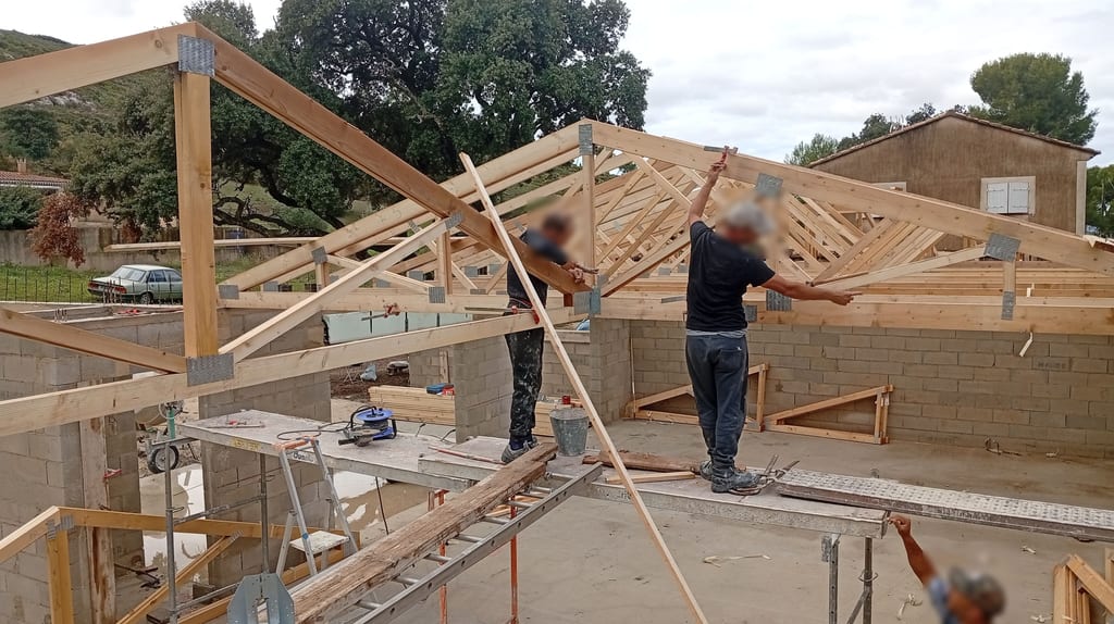 Compagnons sur l'échafaudage alignant les fermettes au cordeau sur une maison plain-pied à Aix-en-Provence